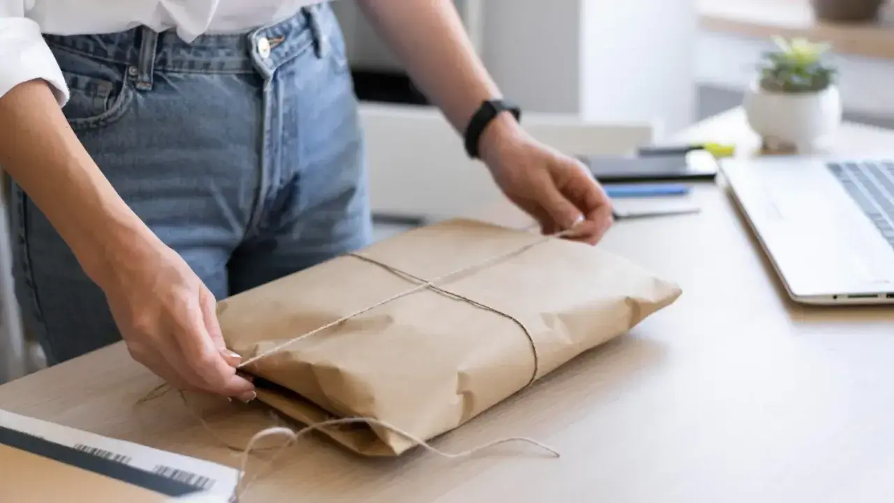 Ręce zawiązują sznurkiem paczkę w brązowym papierze. Gdzie nadać mini paczkę Poczta Polska?