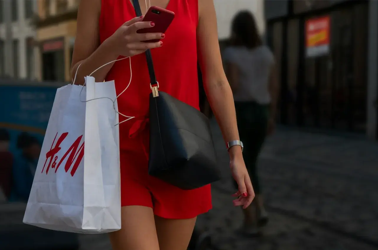 Kobieta w czerwonej sukience trzyma torbę z logo H&M. Zastanawia się, ile dni na zwrot ma zakupiony towar.