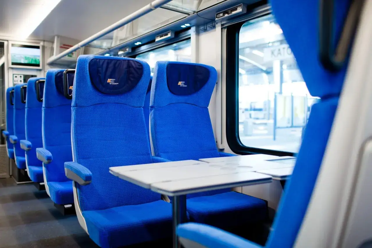 Wygodne, niebieskie fotele w wagonie PKP Intercity. Stolik czeka na pasażerów, którzy wybierają podróż w formie przesyłka konduktorska.