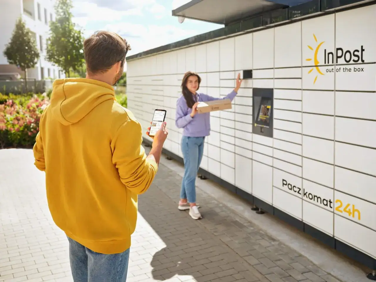 Mężczyzna z telefonem sprawdza, jak najtaniej wysłać paczkę InPost. Kobieta wkłada paczkę do paczkomatu.