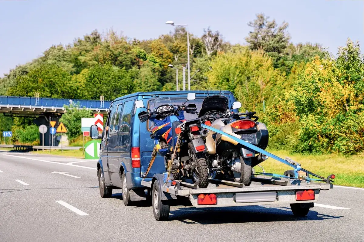 DPD transport motocykla: niebieski van z przyczepą przewozi dwa motocykle.