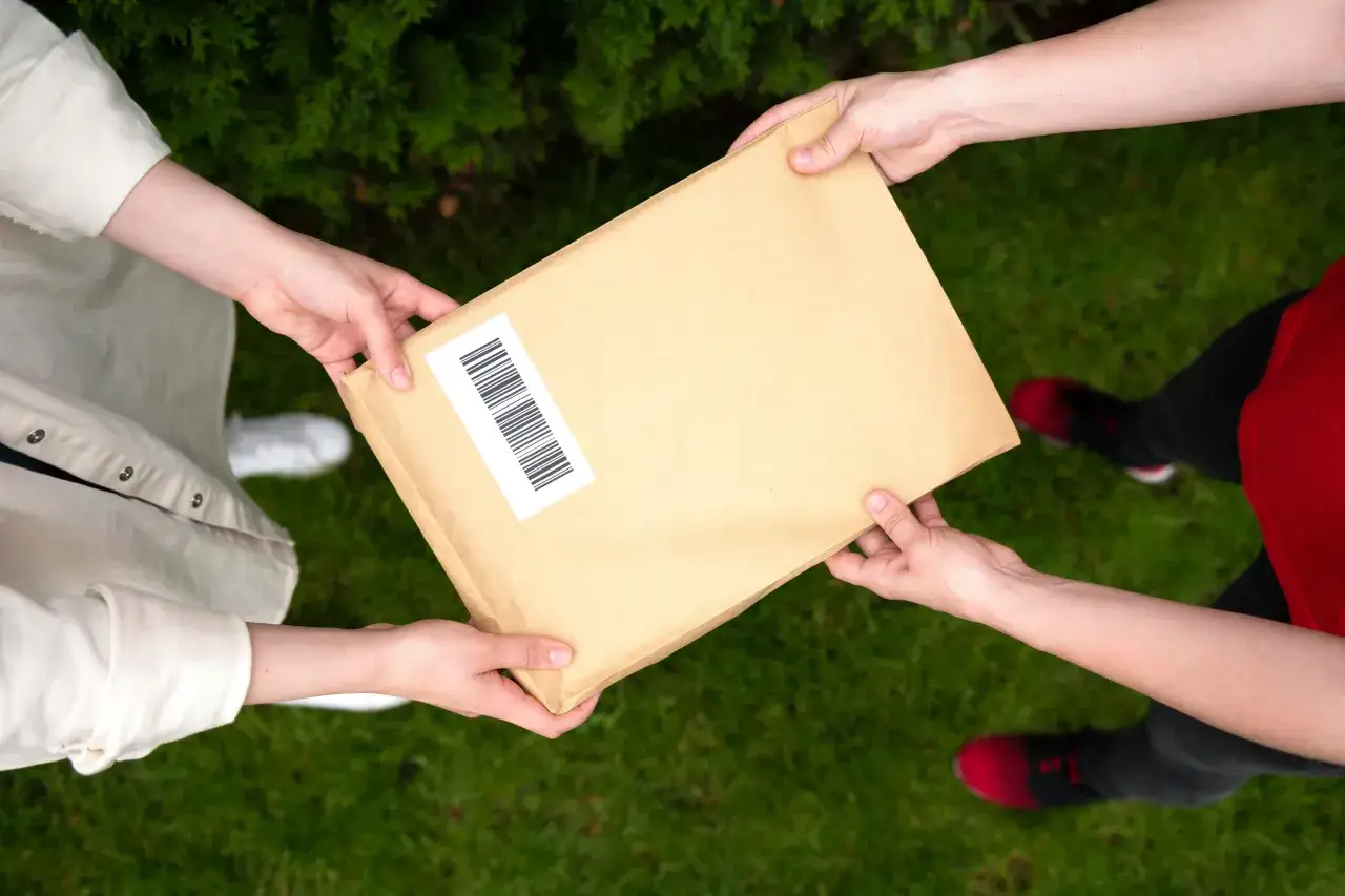 Dwie osoby przekazują sobie paczkę z kodem kreskowym. Może to być początek lub koniec procesu anulowania paczki InPost.